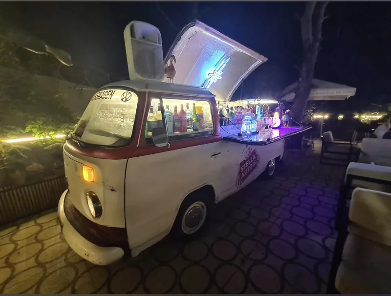 Le Combi Volkswagen transformé en bar, éclairé, sur la terrasse la nuit.
